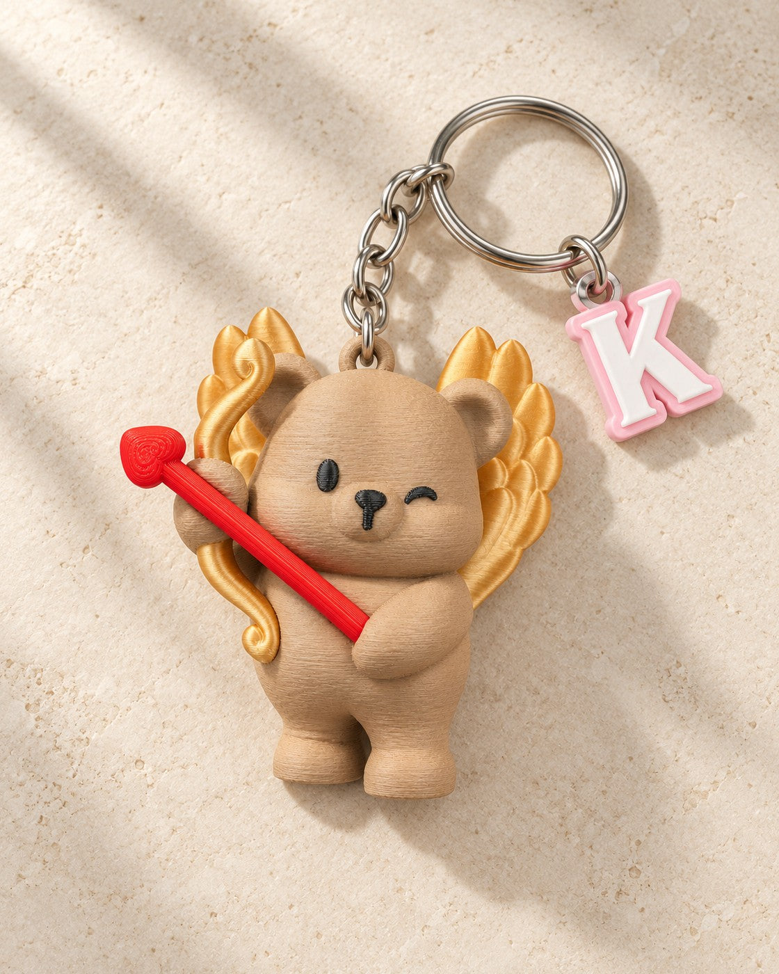 Cupid Cub Initial Keyring on a pale limestone plinth, soft studio light