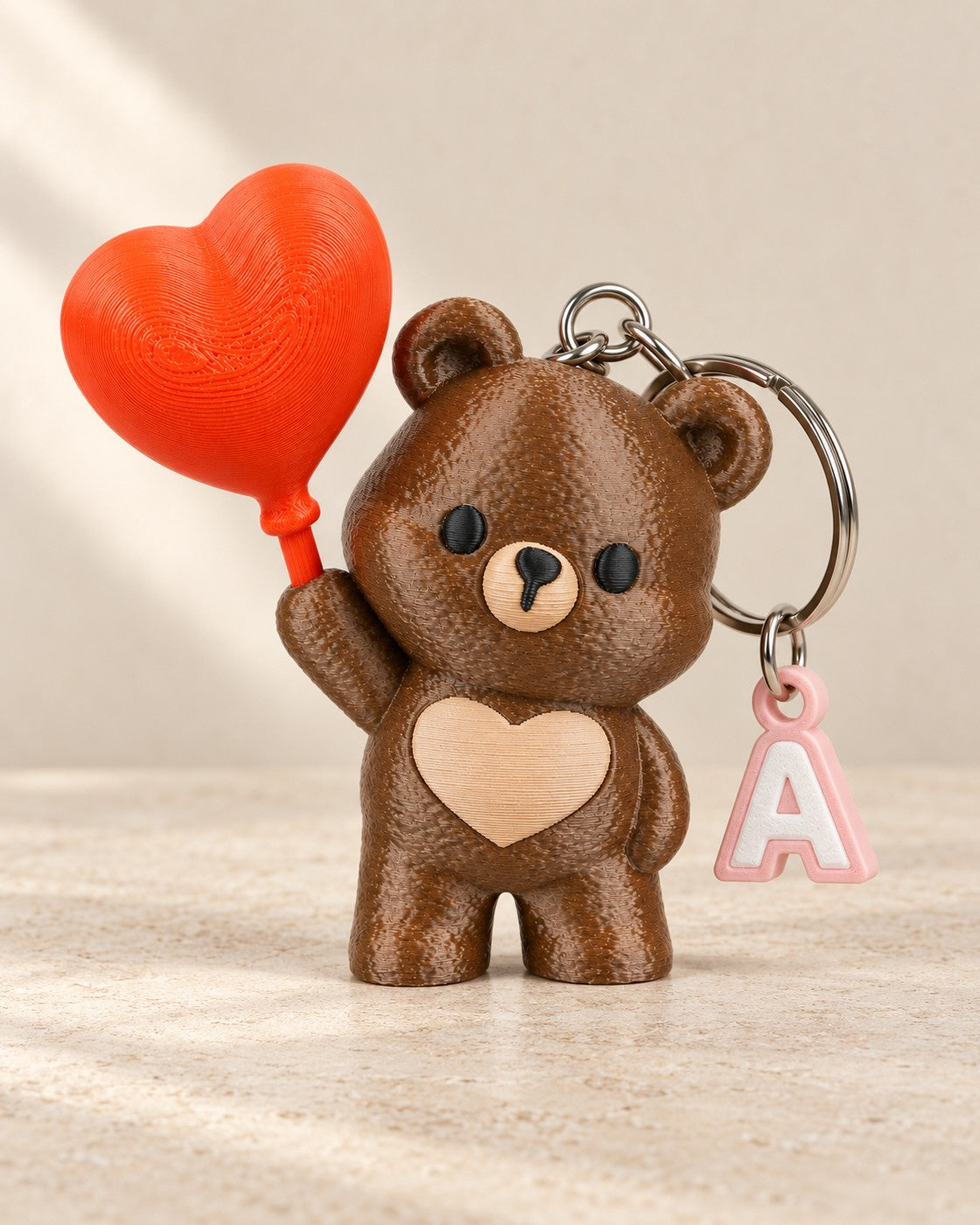 Heart Up Bear Initial Keyring on a pale limestone plinth, soft studio light