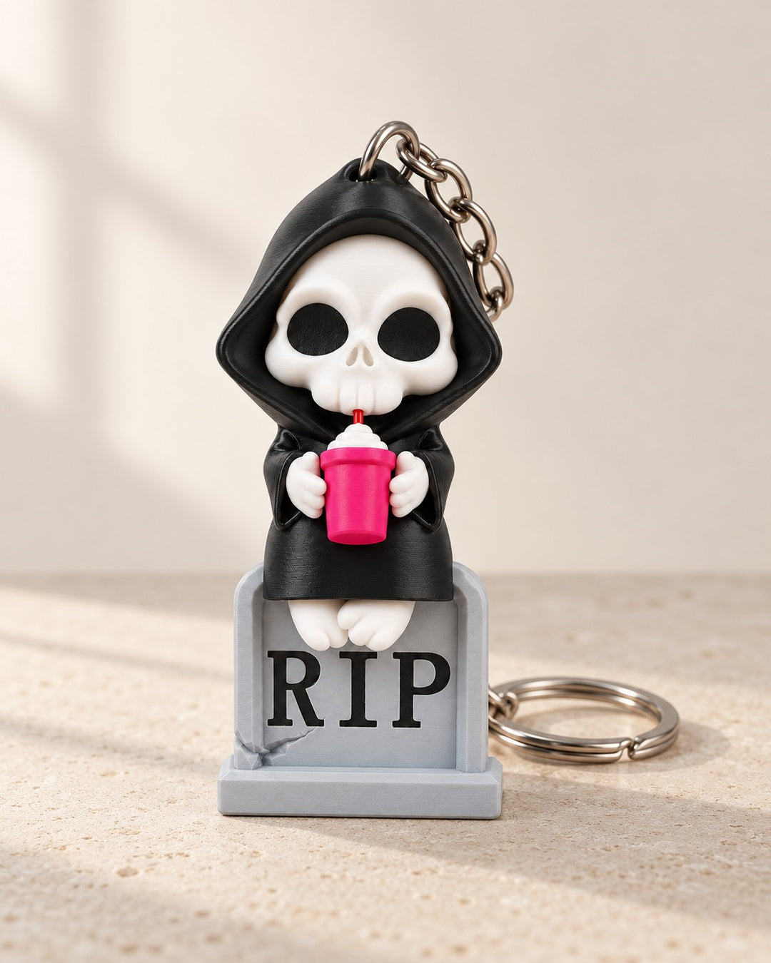Sweet Rest Reaper Keyring: A cute hooded reaper with a pink milkshake, perched on a RIP tombstone