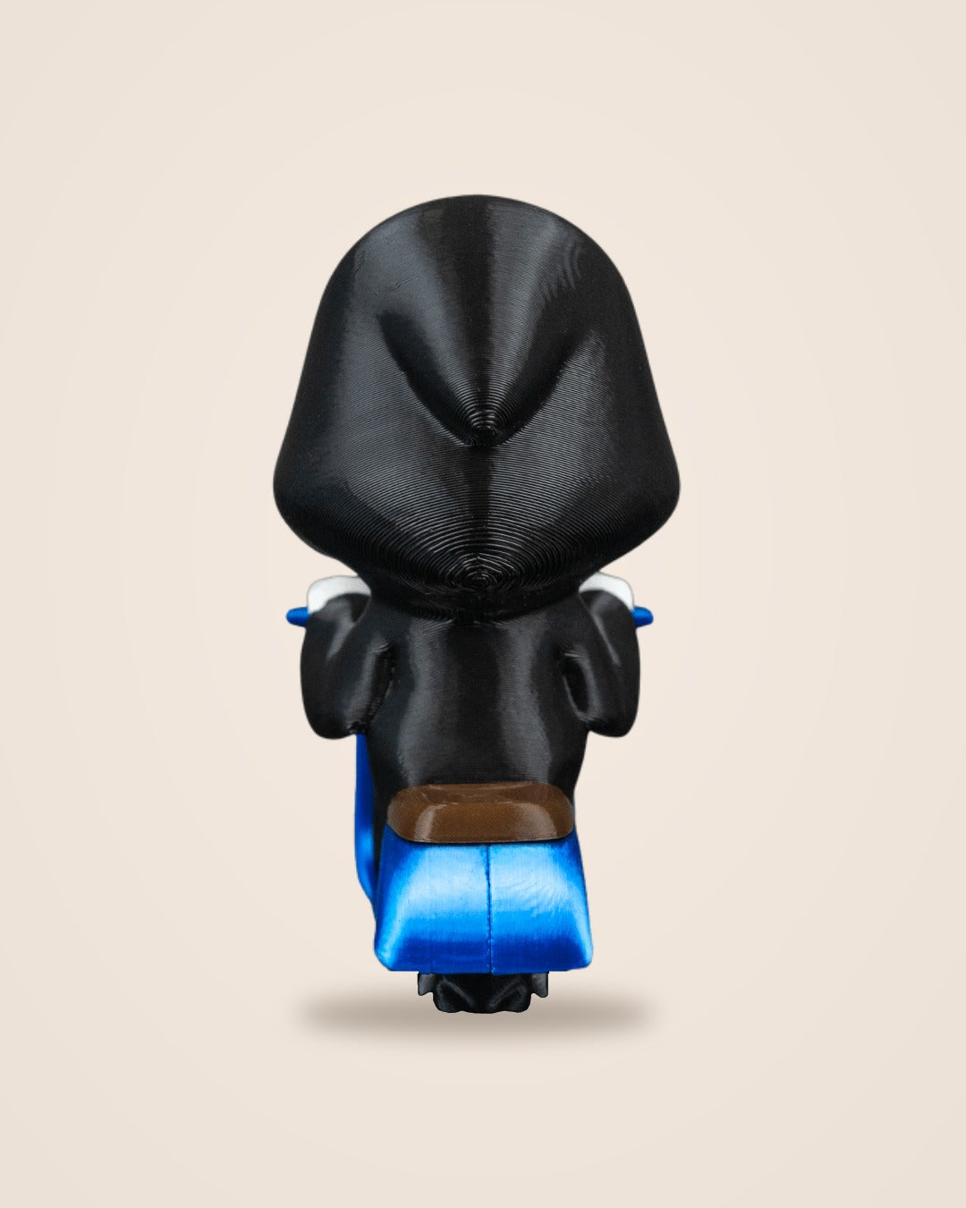 Back view of a hooded Grim Reaper figurine on a blue scooter showing the brown saddle and black rear tyre