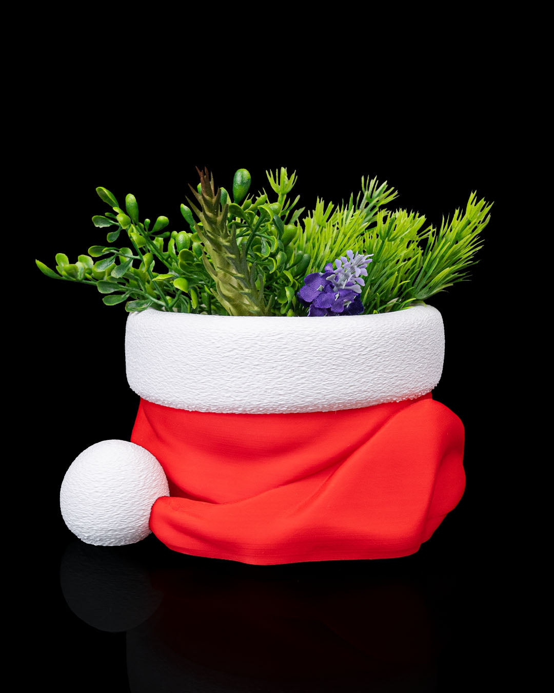 Red and white Santa hat bowl holding green artificial foliage and a small purple flower, with the white pompom at the front left
